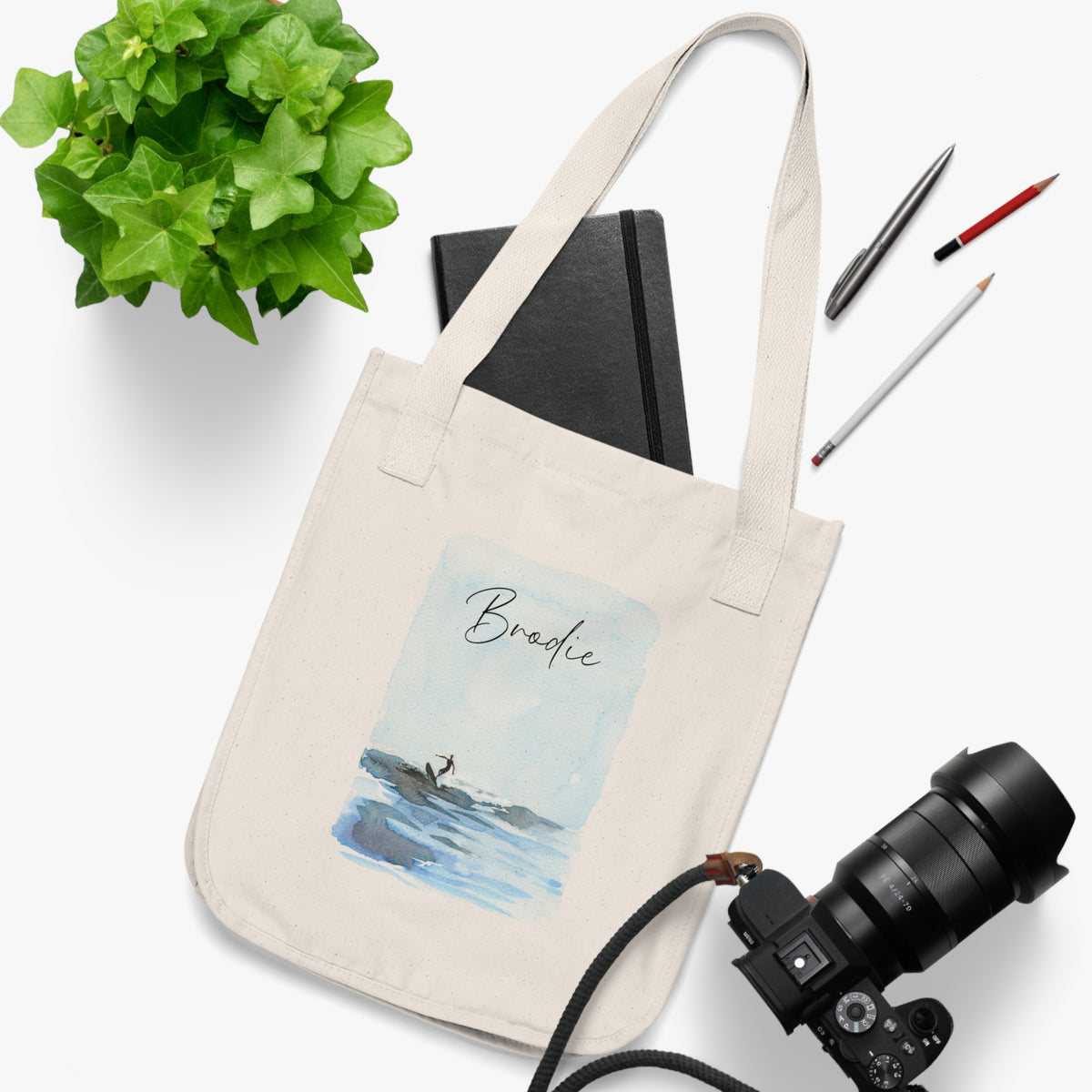An organic cotton canvas tote bag with a printed watercolor illustration of a surfer and custom text. Personalized Surfing Design on Organic Cotton Canvas Tote Bag with customizable text. Perfect on-the-go tote bag for running errands or day trips to the beach. Gift idea for family, friend or yourself. Custom tote bag.