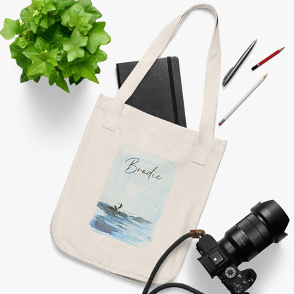 An organic cotton canvas tote bag with a printed watercolor illustration of a surfer and custom text. Personalized Surfing Design on Organic Cotton Canvas Tote Bag with customizable text. Perfect on-the-go tote bag for running errands or day trips to the beach. Gift idea for family, friend or yourself. Custom tote bag.